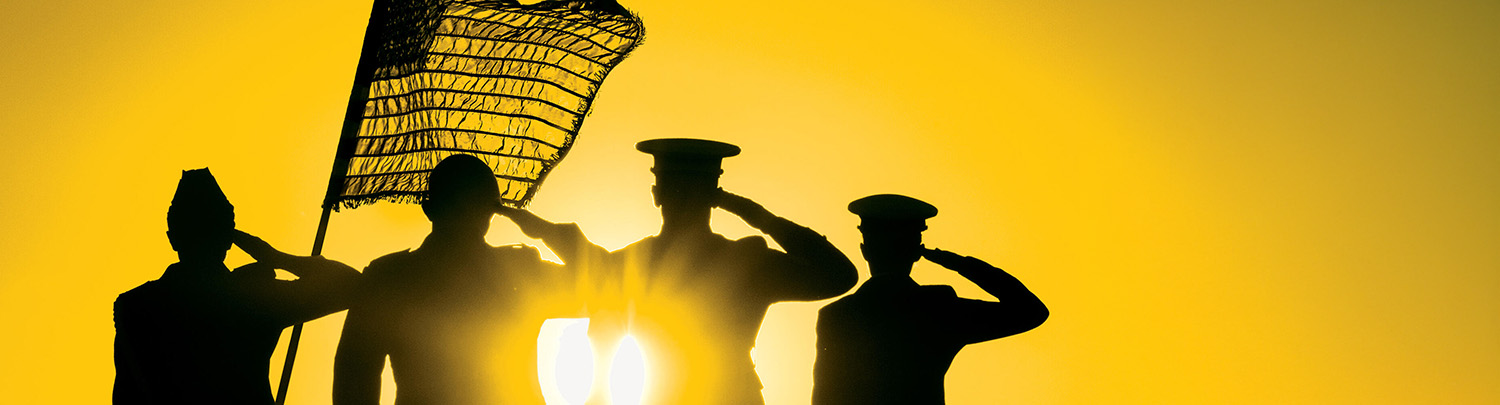 Silhouetted military figures saluting at sunrise or sunset with an American flag.