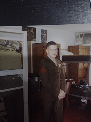 Michael Maisano wearing a military uniform, standing in barracks.