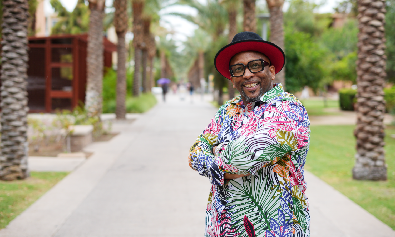 Man with a beard smiling with palm trees and a walking path in the background