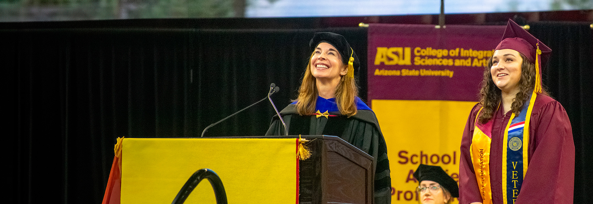 Two women smiling on stage during a graduation ceremony.